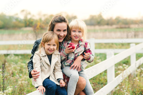 Young mother and her little daughters on a walk at countryside. Happy family together on nature. Relationships, good mood and fashion concept.