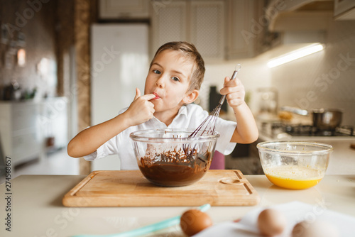 Male kid tastes melted chocolate in a bowl