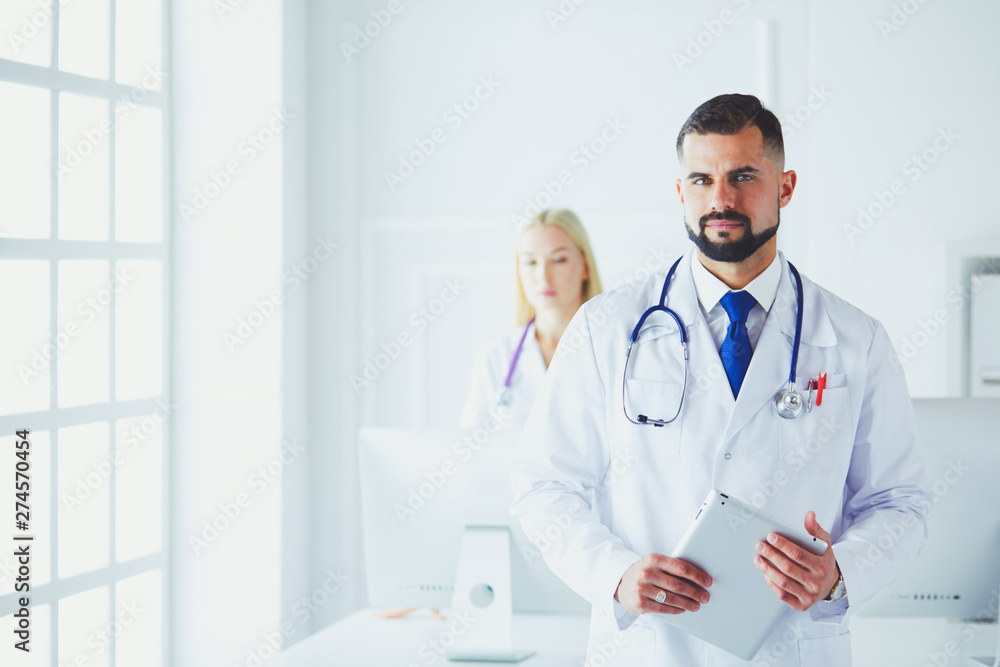 Confident smiling doctor posing and looking at camera with arms crossed, medical staff working on the background Confident smiling doctor posing and looking at camera with arms crossed, medical staff working on the background