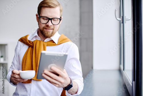 Mid age businessman looking at the tablet and drinking tea in the office
