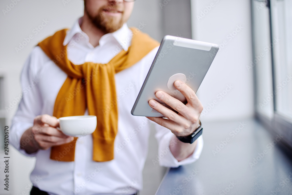 Mid age businessman looking at the tablet and drinking tea in the office Mid age businessman looking at the tablet and drinking tea in the office