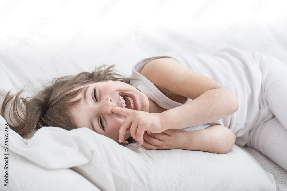 Cute little girl smiling while lying in a cozy white bed Cute little girl smiling while lying in a cozy white bed