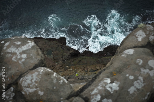View from top point of rocky cliff: raging blue ocean with white foam centered in composition.