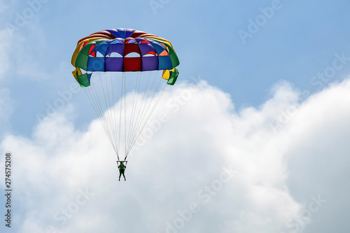 Vacation, extreme sports - colorful parachute over the sky with clouds. One women are flying in the blue sky using multicolored parachute over the sea. Rest on the water. Selective focus. Copy space.