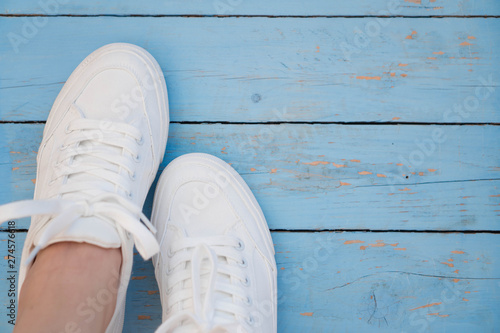 White women's sneakers on a blue boardwalk background. Clean white sneakers in the left of the frame on the blue wooden floor. Trend shoe onthe blue background witn copyspace © SilverOwl