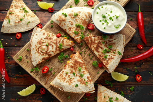 Mexican quesadilla with chicken, corn, black beans, cheese, vegetables, lime and yogurt sauce on wooden board photo