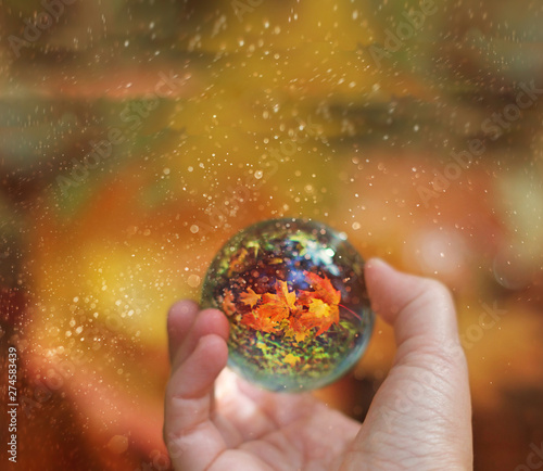 transparent glass globe with reflection in hand. autumn season. beautiful still life with glass ball on nature background. mystical art image. copy space. 