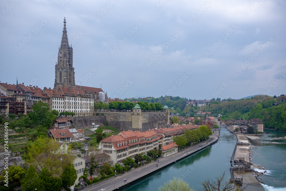 Beautiful view of aare river with Bern Munster, landmark of Bern, and charming building from Kirchenfeld bridge on cloudy blue sky background