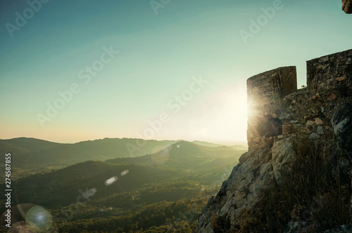 Fototapeta Stone wall with merlons in Castle over hill on sundown