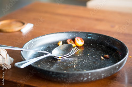 Empty of black ceramic dish with fork and spoon on wooden table