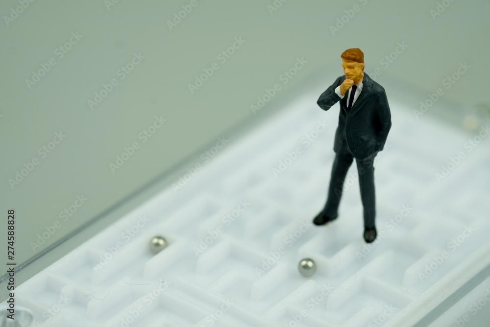 Miniature people businessman standing on maze background Miniature people businessman standing on maze background