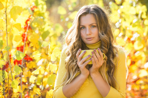 Closeup portrait of young beautiful woman on autumn background with cup of coffee. Female on fall background outdoors.