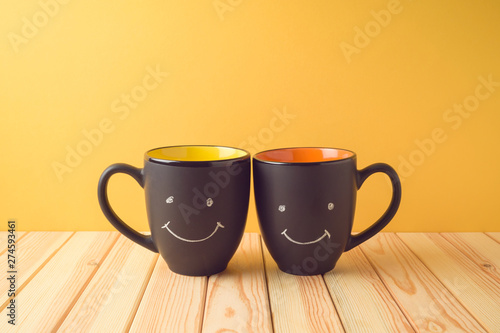 Chalkboard coffee mugs on wooden table with funny cute faces. Friendship day concept