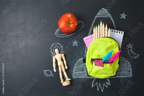 Back to school concept with small bag backpack, school supplies and rocket sketch over chalkboad background. Top view from above photo