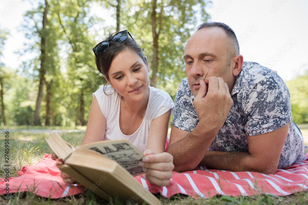 middle aged couple layed on blanket looking at book middle aged couple layed on blanket looking at book