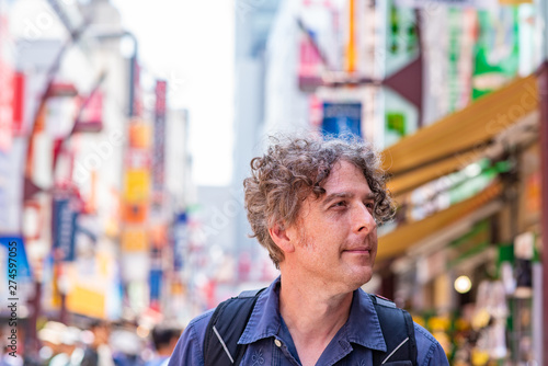 A middle aged man enjoys traveling in Tokyo, Japan, at the Ameyoko Market in Asakusa, on a beautiful day. Beautiful market lights blurred in the background.