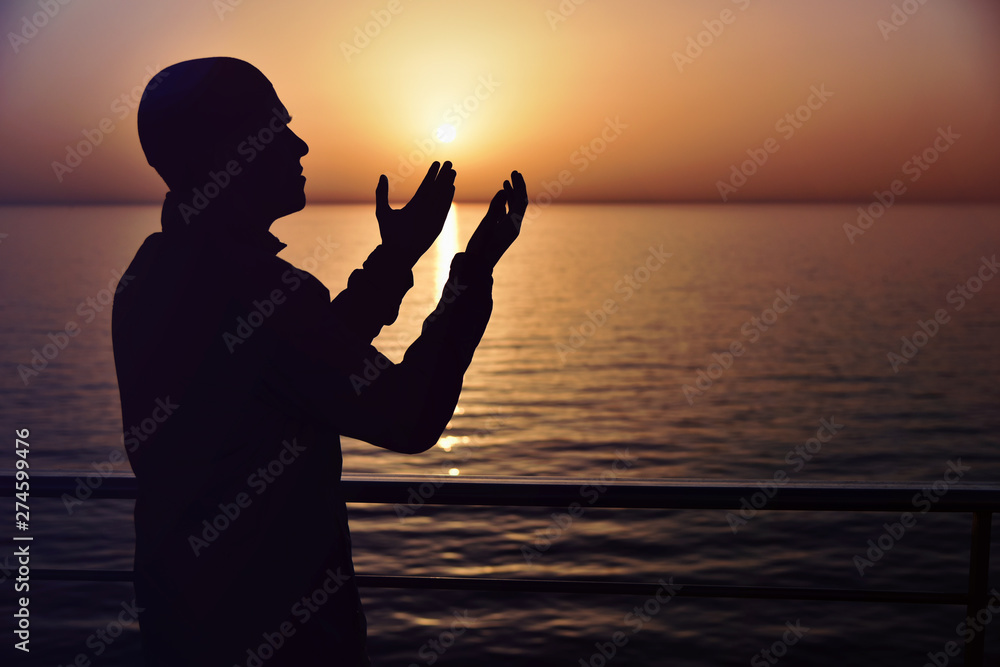 Muslim prayer in the ship praying at sunset with hands up. A silhouette of islamic praying at sunset fom the big ship.