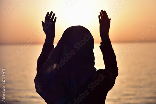 Muslim woman praying in the ship praying at sunset with hands up. A silhouette of islamicwoman praying at sunset fom the big ship.
