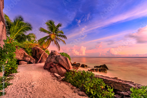 Anse Source d'Argent in Seychelles, La Digue with dramatic colorful sky at eveing. Shaped rock stone of granite, palm trees and seashore. Source d'Argent Beach paradise of Seychelles. Long exposition.