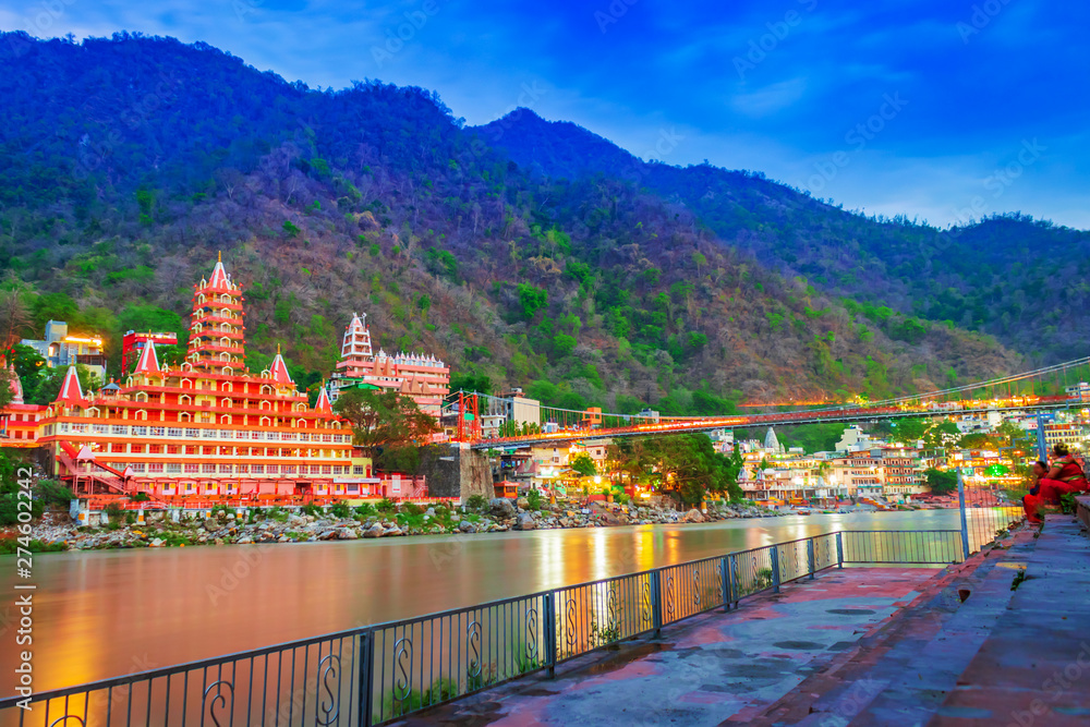  River Ganges, the famous bridge Laxman Jhula  surrounded by temples and mountains around in rishikesh, India 