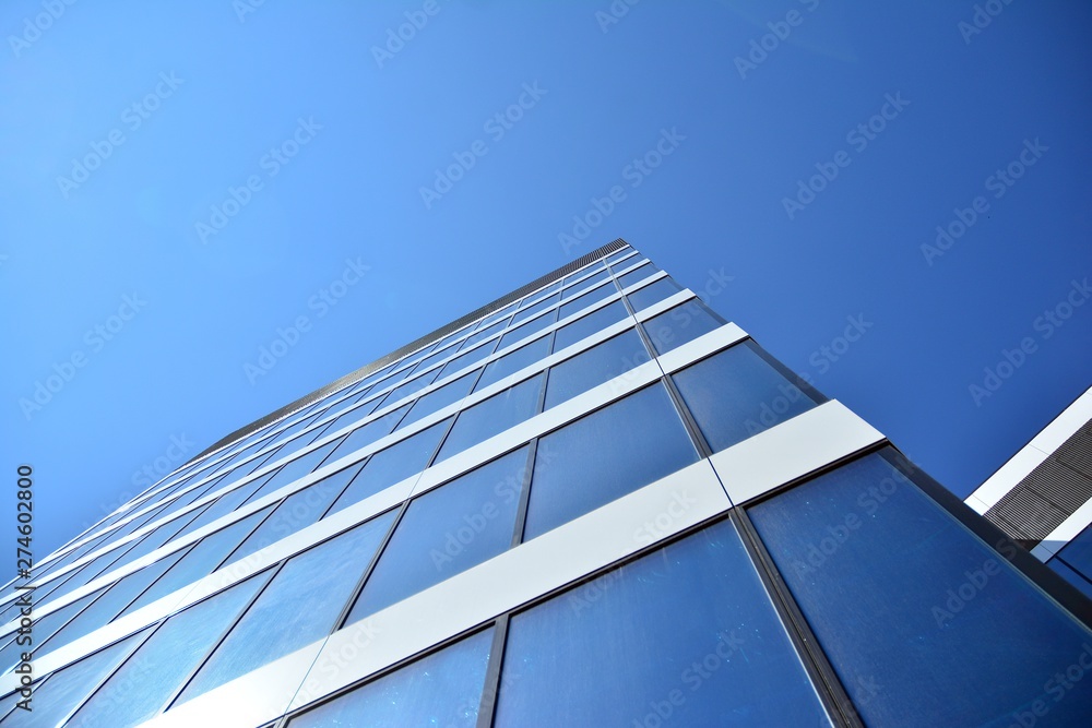 New office building in business center. Wall made of steel and glass with blue sky.  - obrazy, fototapety, plakaty 