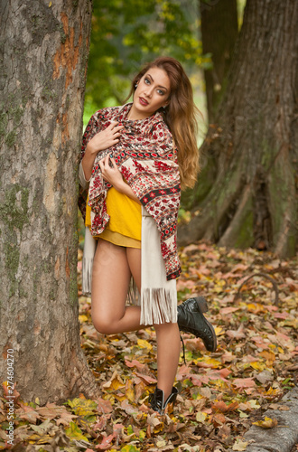 Happy Portrait fashion of a beautiful young Caucasian woman with a scarf,long legs and yellow pullover in autumn park,red green yellow threes. Autumn, season and people concept.Autumn lifestyle
