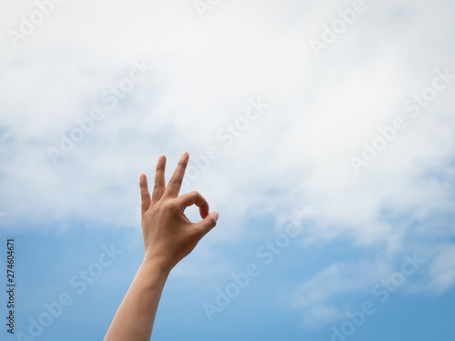 Okey. Woman hand OK sign against with blue sky and white clouds.