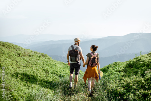 Photos Beautiful couple walking with backpacks on the green meadow, while traveling high in the mountains during the summer time