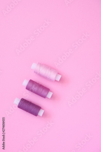 Sewing thread kit of lilac  pink  violet  crimson  sewing thread on a pink paper backgroun  copy space for text. Top view  flat lay.
