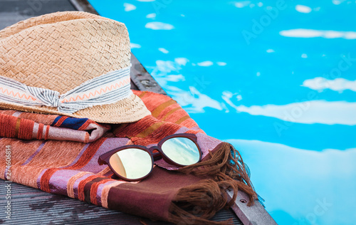 Vintage summer wicker straw beach hat, sun glasses, cover-up beachwear wrap near swimming pool, tropical background.