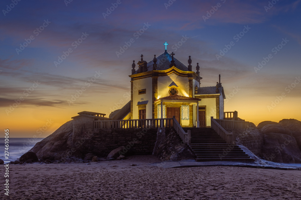 Senhor da pedra - chapel in the cliffs by the sea at sunset, Porto district, Portugal.