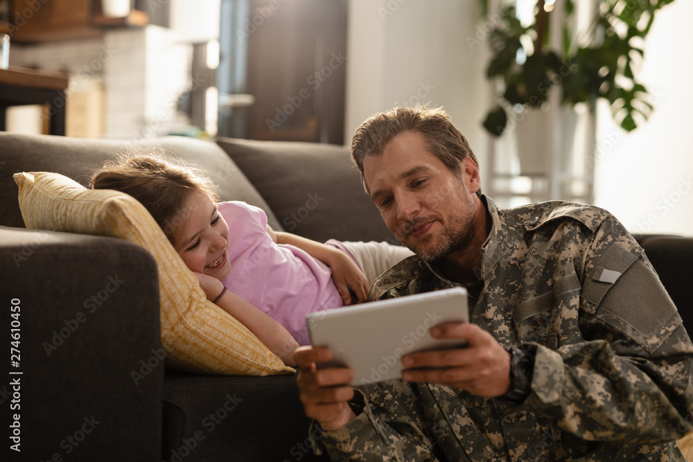 Happy army soldier and his daughter using touchpad in the living room. Happy army soldier and his daughter using touchpad in the living room.
