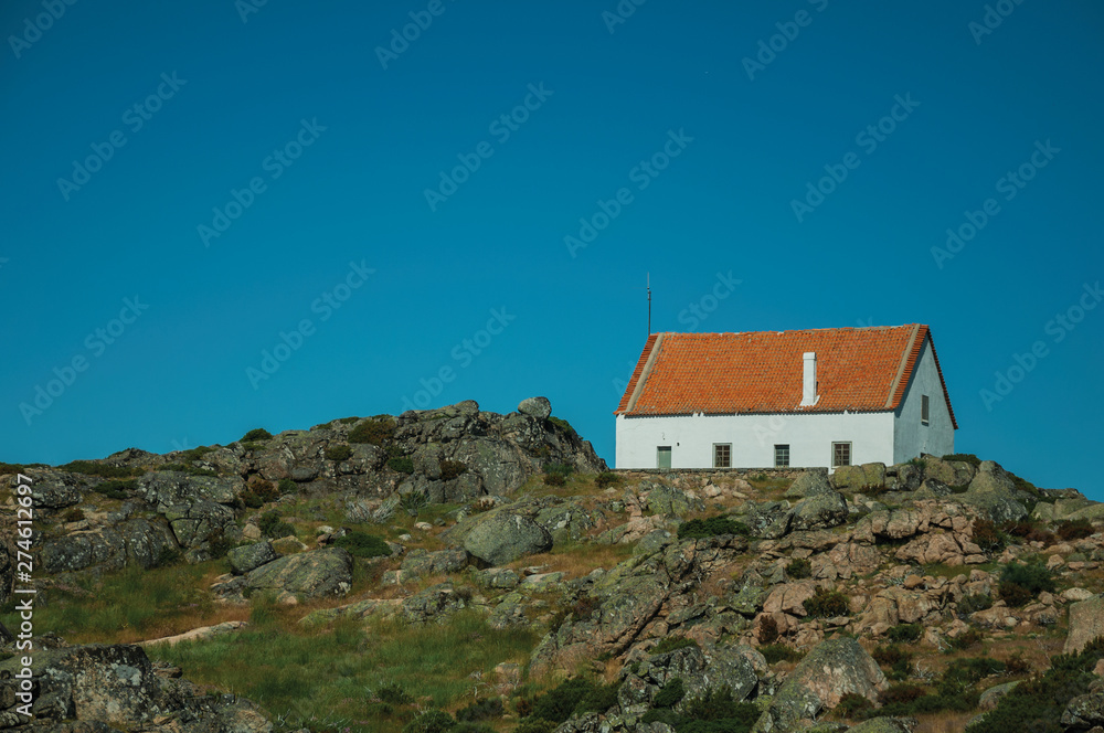 House on top of hilly landscape with bushes and rocks