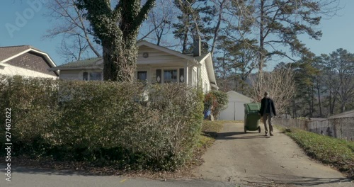 Man walking a trash can down to the end of a driveway in the winter
