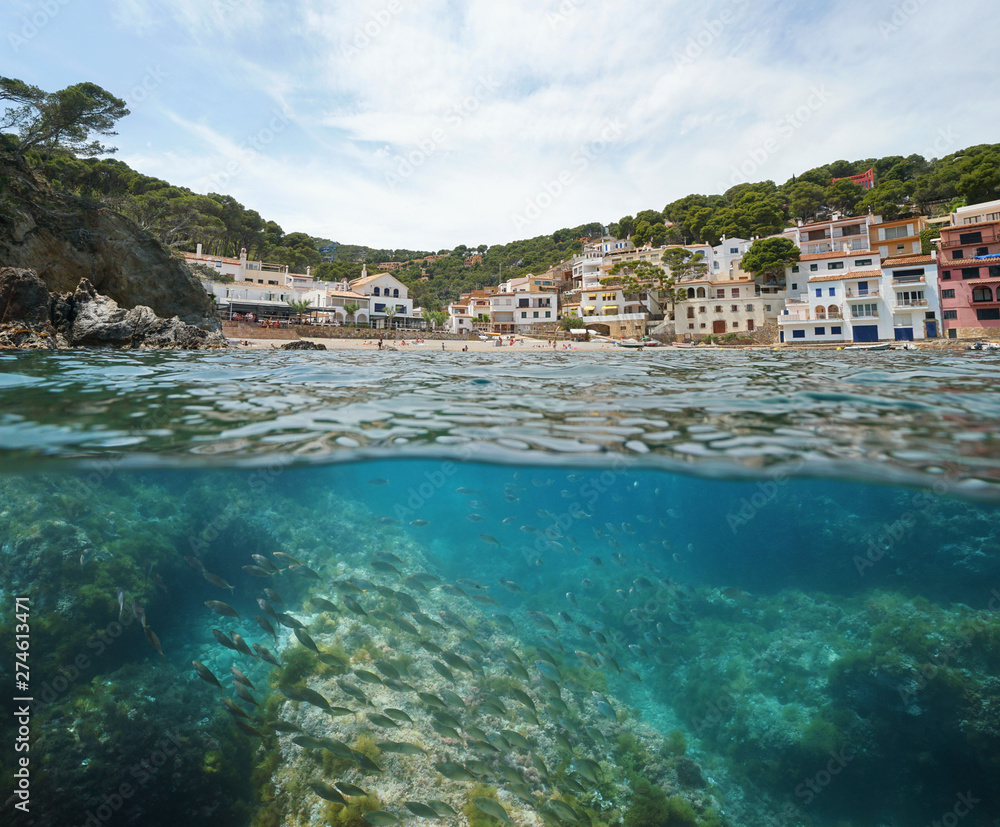 Spain coastal village with beach and fish underwater, Mediterranean sea, Sa Tuna cove, Begur, Costa Brava, Catalonia, split view half over and under water