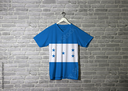 Honduras flag on shirt and hanging on the wall with brick pattern wallpaper. © Achisatha