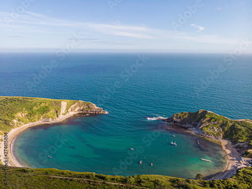 A view of the Lulworth Cove along the Jurrassic Coast in Dorset under a majestic blue sky and some white clouds.