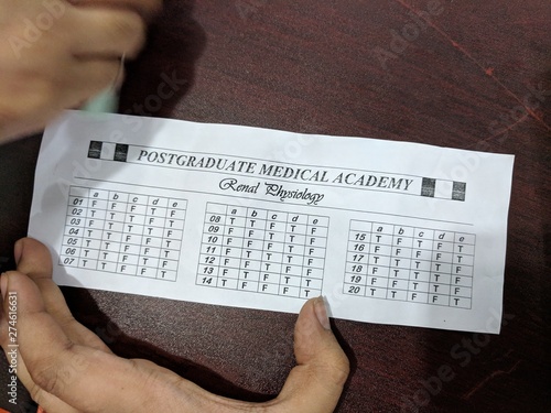 hand with mcq answer sheet and pen on table