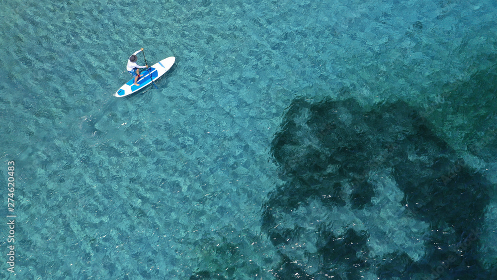 Aerial photo of unidentified fit man practising SUP or Stand Up Paddle in tropical exotic destination island with turquoise sea