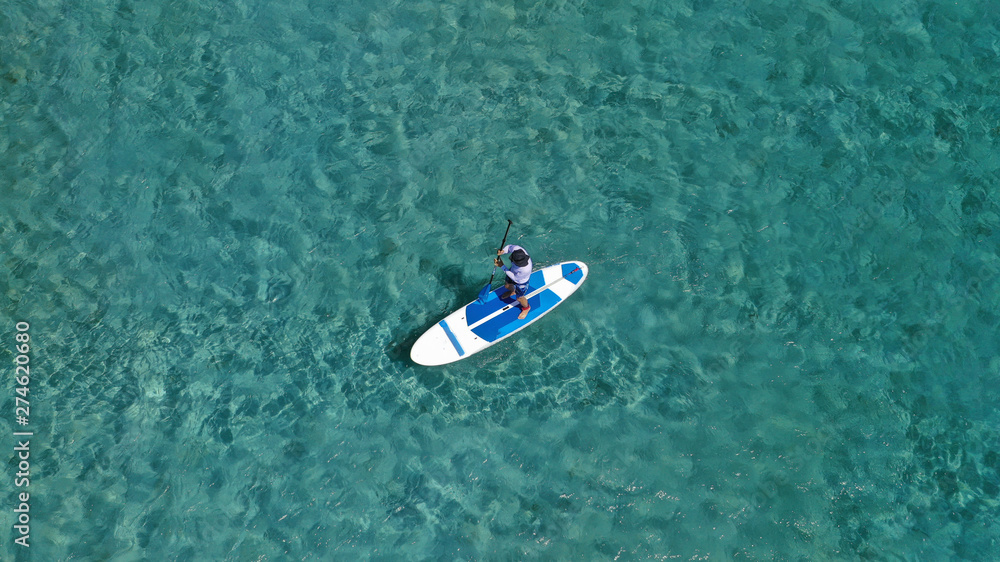 Aerial photo of unidentified fit man practising SUP or Stand Up Paddle in tropical exotic destination island with turquoise sea