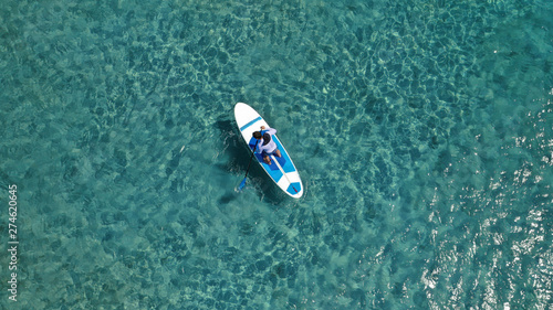 Aerial photo of unidentified fit man practising SUP or Stand Up Paddle in tropical exotic destination island with turquoise sea