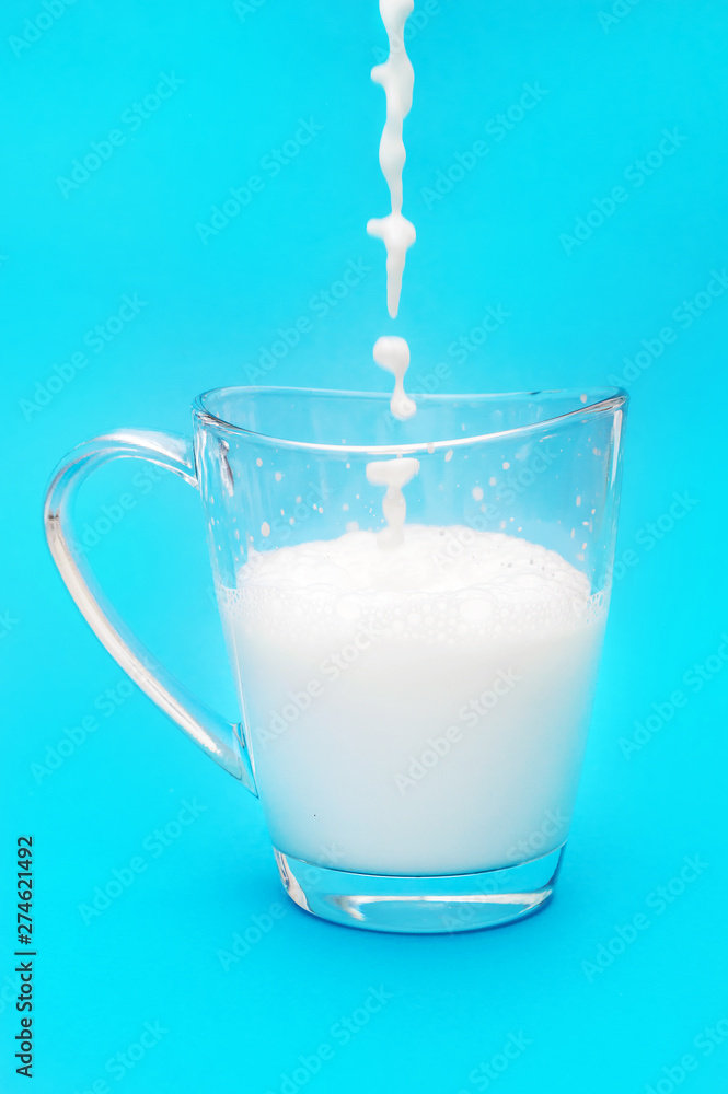 Milk pouring into the glass cup on blue background. Milk pouring into the glass cup on blue background.