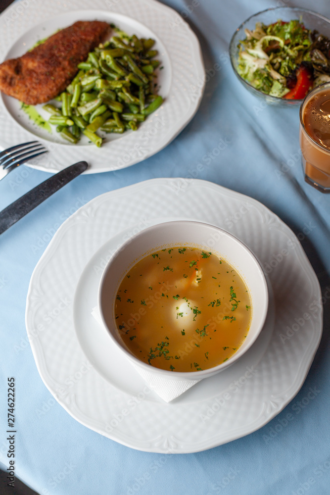 Three course substantial set meal on a blue tablecloth: hot chicken noodle soup, chicken schnitzel with green beans green broccoli salad and a cup of coffee Three course substantial set meal on a blue tablecloth: hot chicken noodle soup, chicken schnitzel with green beans green broccoli salad and a cup of coffee