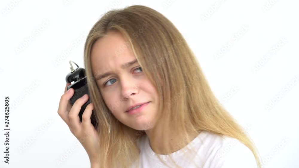 Portrait of a happy cute teenage girl with long flowing hair on a white background who is holding a Desk clock and puts it to your ear to hear if it's on? Close up. Portrait of a happy cute teenage girl with long flowing hair on a white background who is holding a Desk clock and puts it to your ear to hear if it's on? Close up.
