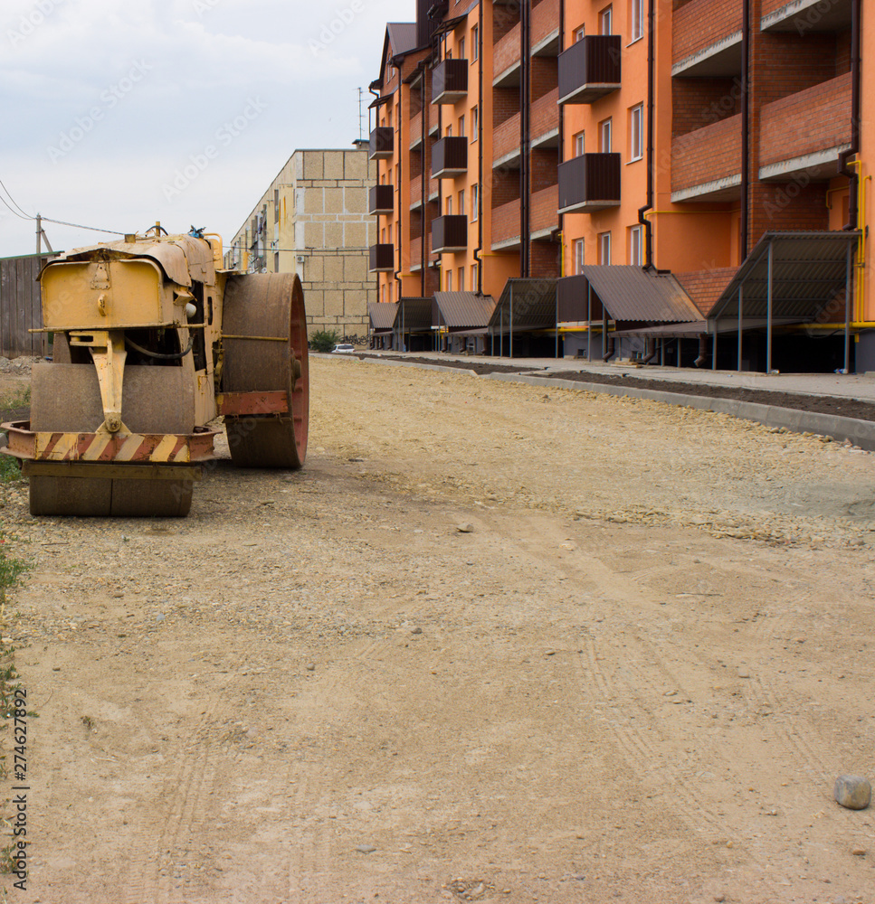 Old paver on the background of the road, prepared for laying asphalt and a new house. Old paver on the background of the road, prepared for laying asphalt and a new house.