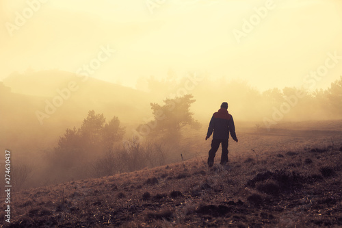 Alushta, Republic of Crimea - March 1, 2019: Alone tourist goes through the mist sunset sunlight across the mountain Demerdzhi