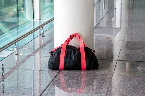 Suspicious black and red bag left unattended in an empty hall. Concept of terrorism and public safety. Dangerous ownerless derelict luggage.