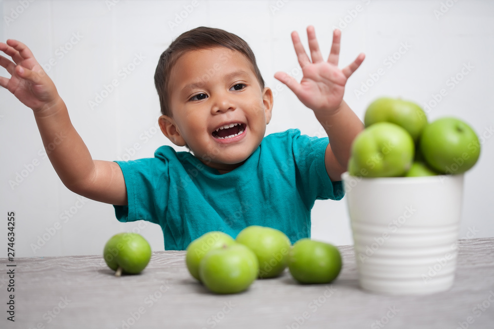 A young boy expressing his joy for fresh fruits, with arms up in the air and playing with a bucket of green apples. A young boy expressing his joy for fresh fruits, with arms up in the air and playing with a bucket of green apples.