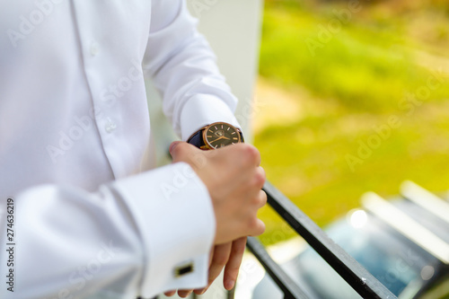 Man in the white shirt wearing the watch on the balcony of your room in the background of the garden. The groom is going to the wedding. The entrepreneur is preparing for the working day.