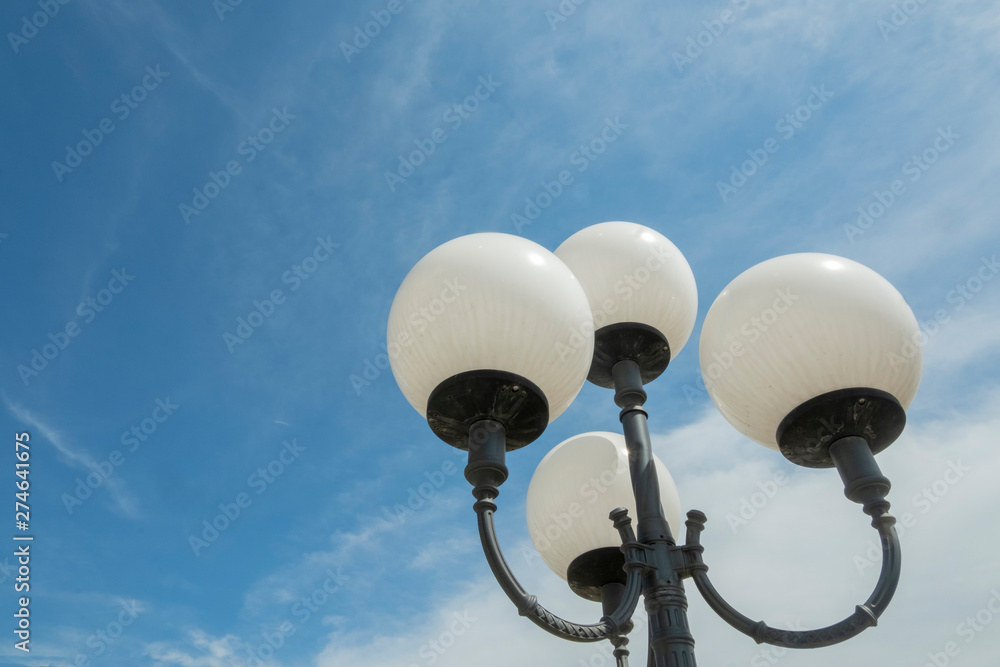 Round street lights in white. Blue sky with cirrus clouds. Metal candle holders. Round street lights in white. Blue sky with cirrus clouds. Metal candle holders.
